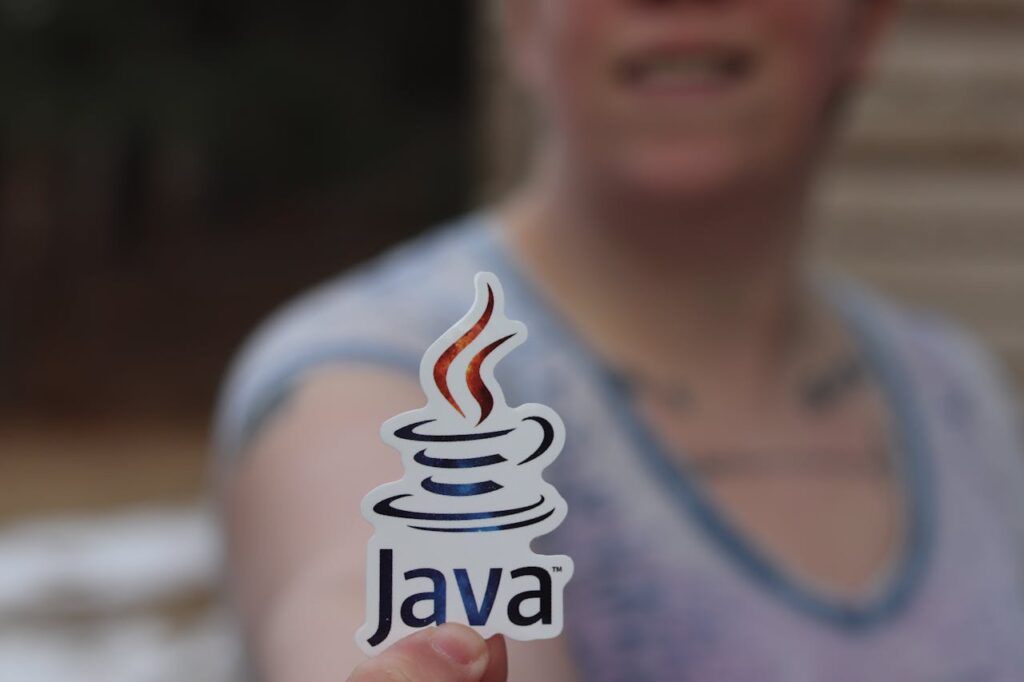 A person holding a Java sticker in an outdoor setting, focus on the sticker.