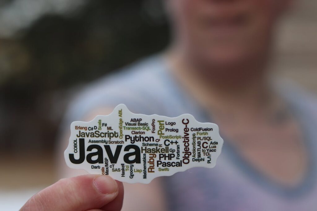 Close-up of a person holding a sticker with various programming languages listed on it.